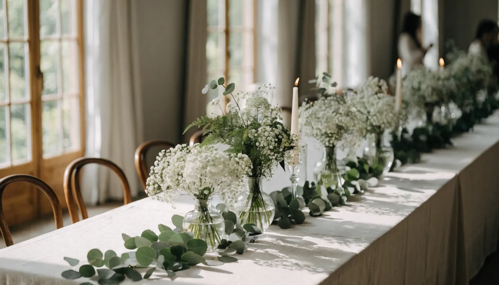 Lange Tafel mit niedrigen weiß-grünen Blumengestecken, Kerzen und Eukalyptusgirlande