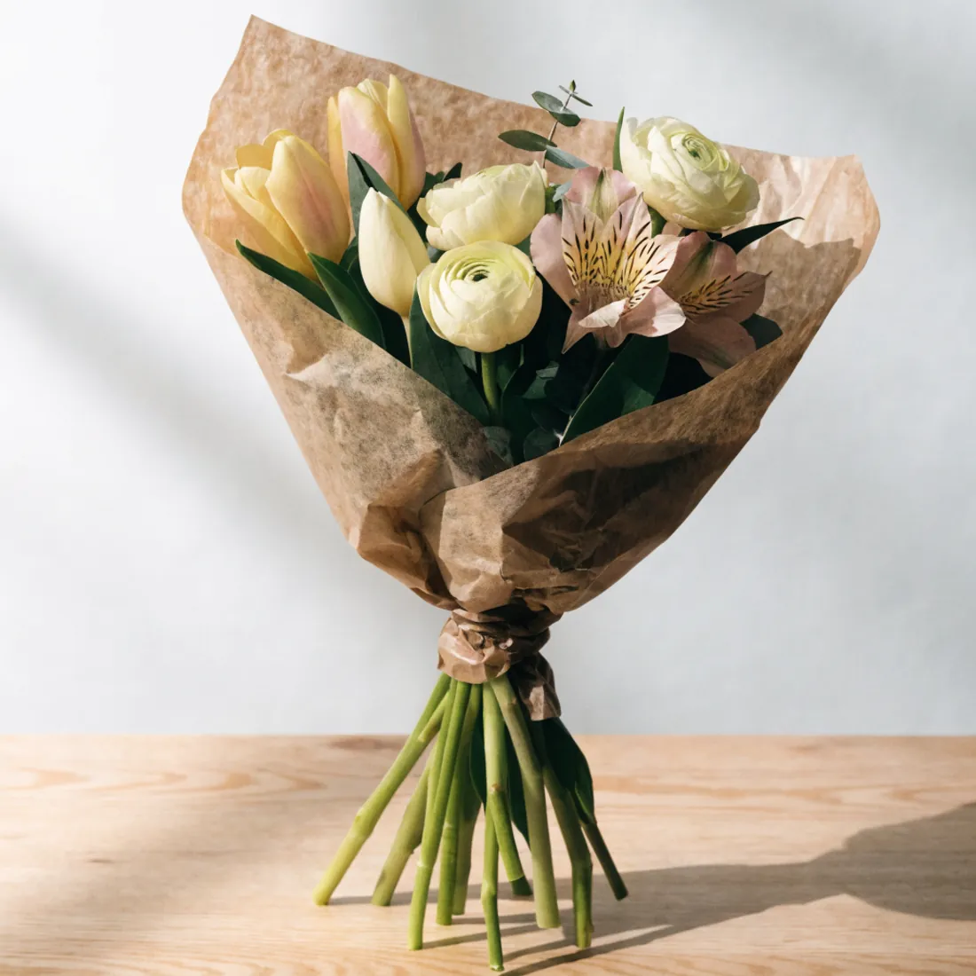 Handgebundener Saisonstrauß in Kraftpapier mit Tulpen, Ranunkeln und Grün